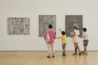 A family of four stands in front of three black and white paintings by Jack Whitten